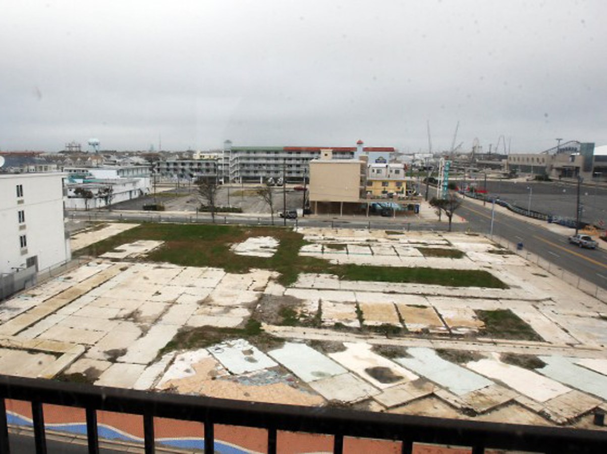 View of vacant lot with grass sections intermixed among larger area of cement foundation.