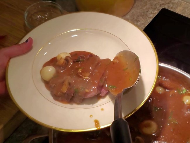 Plate of beef with sauce being served from a stove on a pan