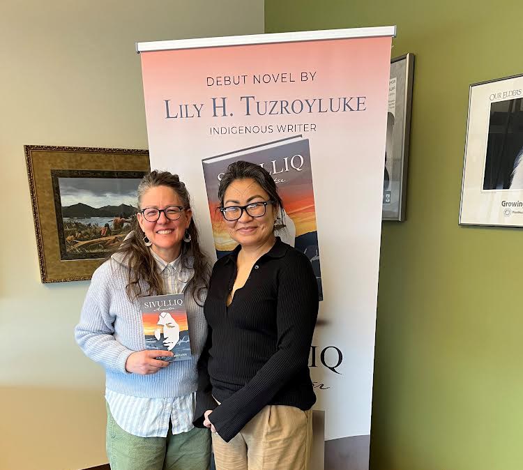 Two women standing in front of a sign that says, "debut novel by Lily H Tuzroyluke"