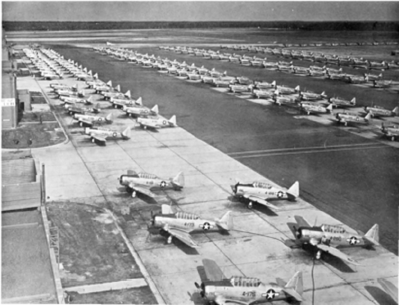 WWII planes lined up on a tarmac with hanger in the background