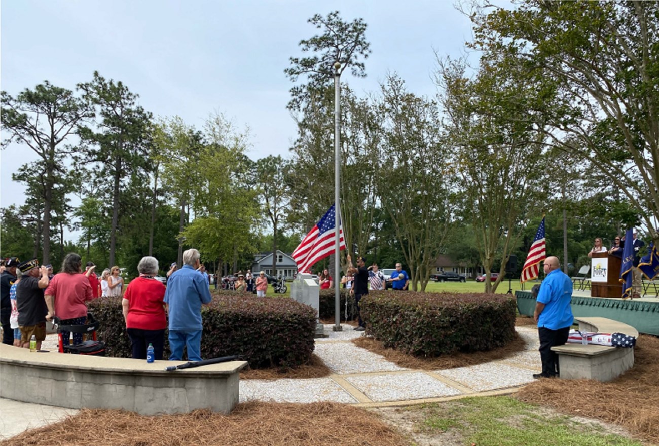 people gathered around a flagpole and stone markers watching flag being raised