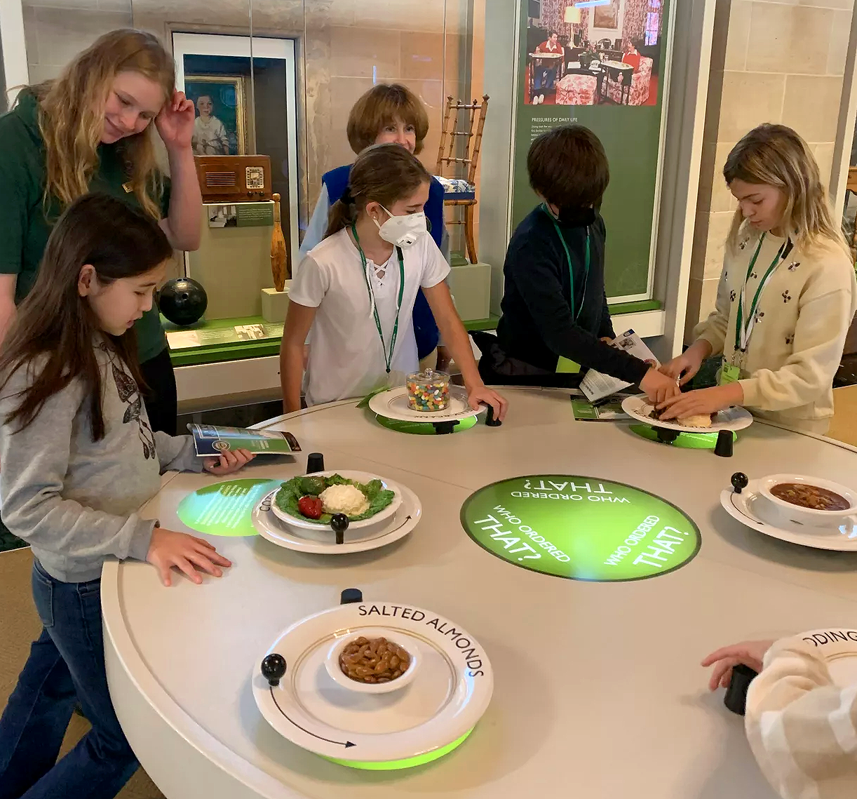 Children stand around a table while examining models of dishes and foods