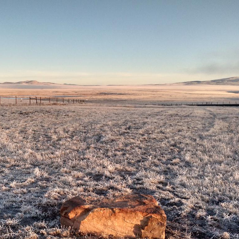 A vast grassland valley is covered in frost in the early morning.