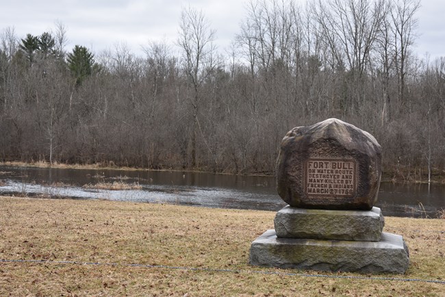 A round boulder on a stone pedestal with a metal plaque reads “Fort Bull- on water route destroyed and many killed by French and Indians, March 27, 1756.” 