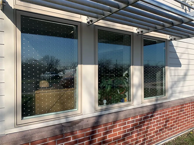 Bay of three windows, each covered in perfectly spaced patterns of small white squares.