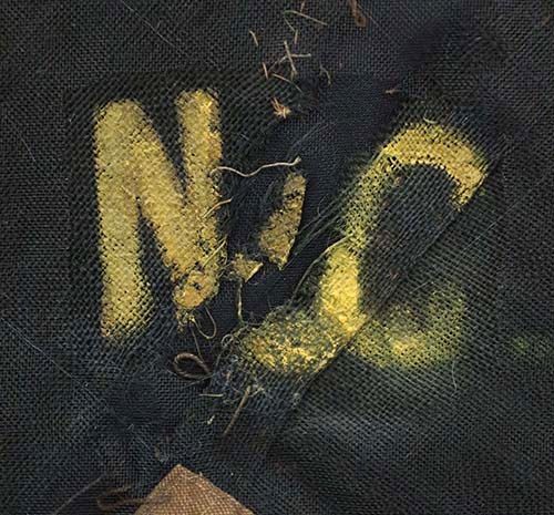 A close-up photo of the letters "NC" panted in yellow over black fabric.