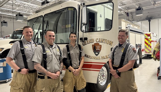 Four men smile in front of a fire engine in an engine bay.