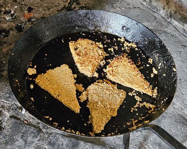 Iron skillet with four thin triangle-shaped golden cakes.