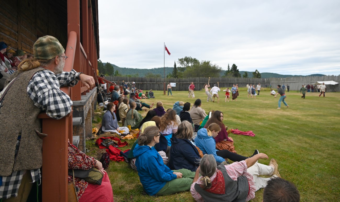 A crowd sitting on the Great Hall lawn watching a lacrosse game