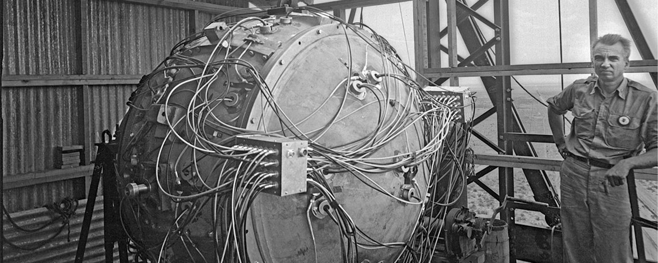 A man is pictured next to a large metal orb with wires surrounding the orb.