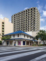 A small vernacular building on a corner with a modern skyscraper behind.