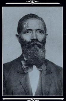 Black and White photo showing a man from the waist up staring to the right with his mouth in a neutral line. He is wearing a suit jacket, bow tie, and vest.