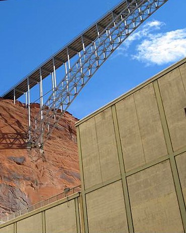 Sheer beige walls of Glen Canyon Dam are topped by a silver bridge