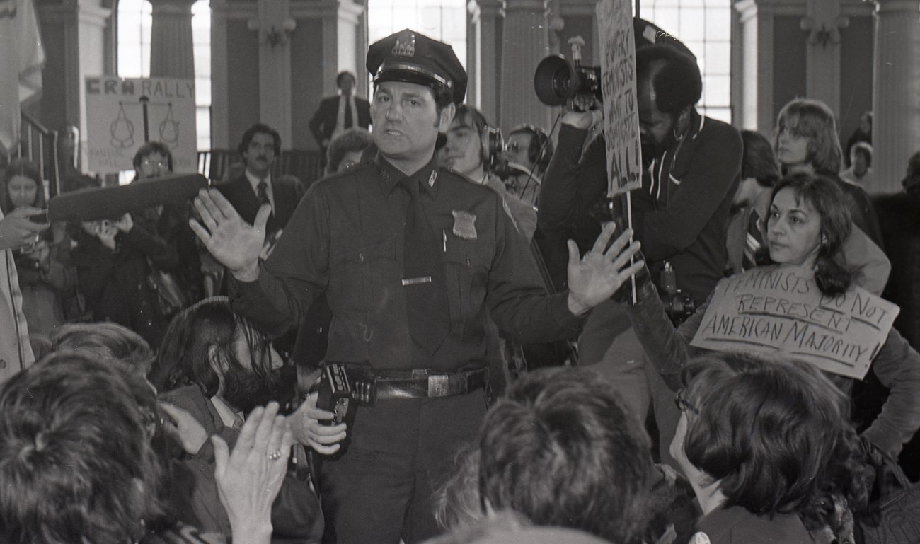 Black and white photo of a Boston Police Officer calming the crowds inside Faneuil Hall