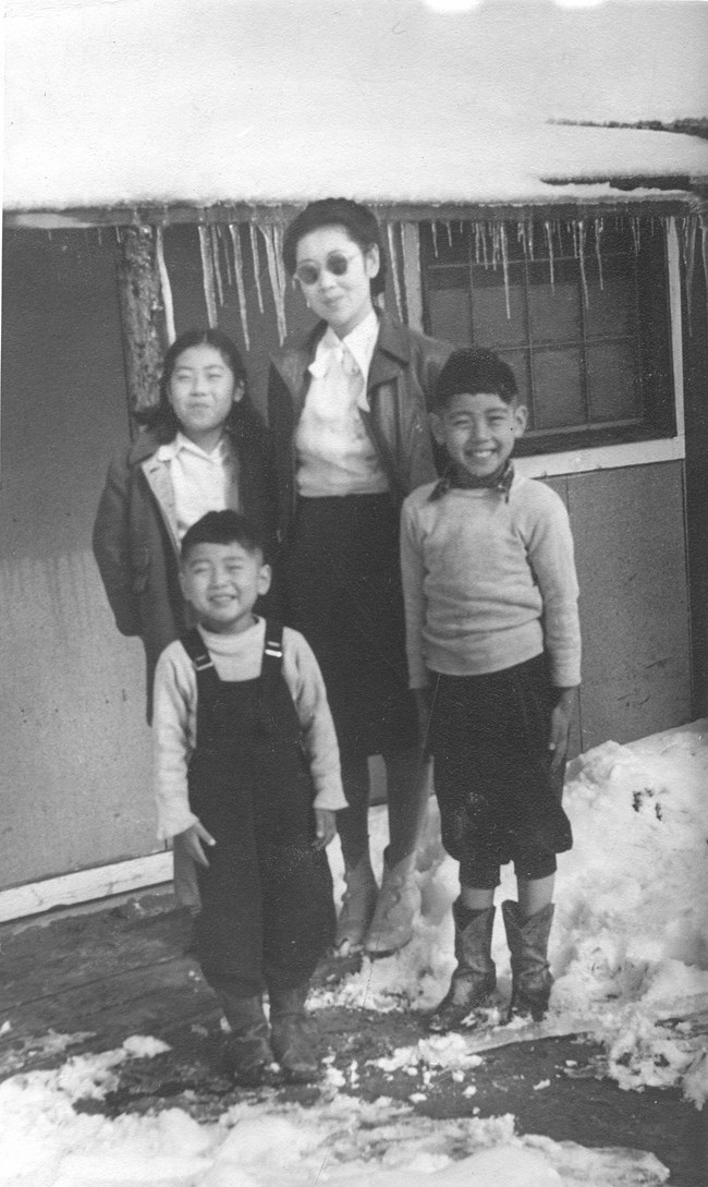 A Japanese American woman with her three children standing outside a barrack in winter.