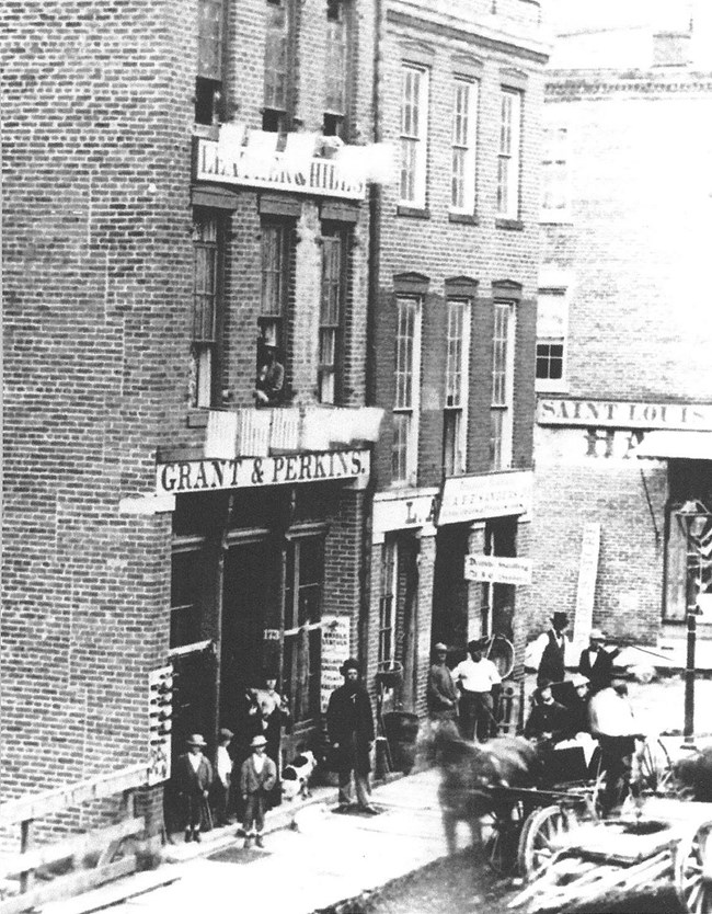 black and white photo of tall brick building with people standing by doorway