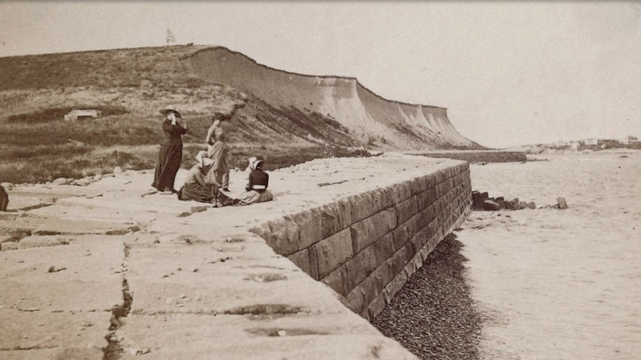 four women sit on the edge of a seawall on Great Brewster Island.