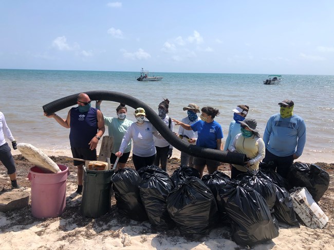line of people on the beach with bags of trash and a long plastic pipe