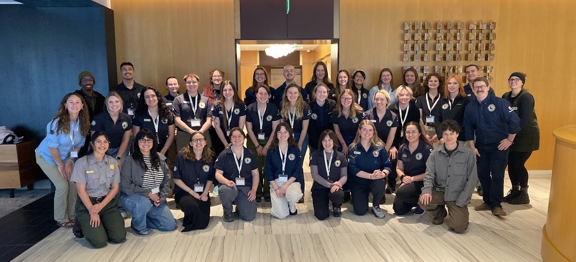 A group of Community Volunteer Ambassadors in blue uniform shirts pose for a photo in a lobby of a visitor center.