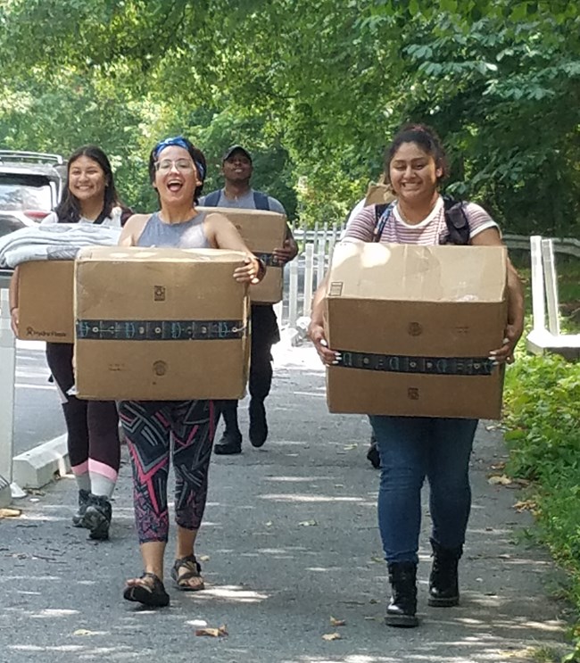 Hispanic Access Foundation Fellows and staff walking towards the campsite carrying cardboard boxes with camping gear inside them.