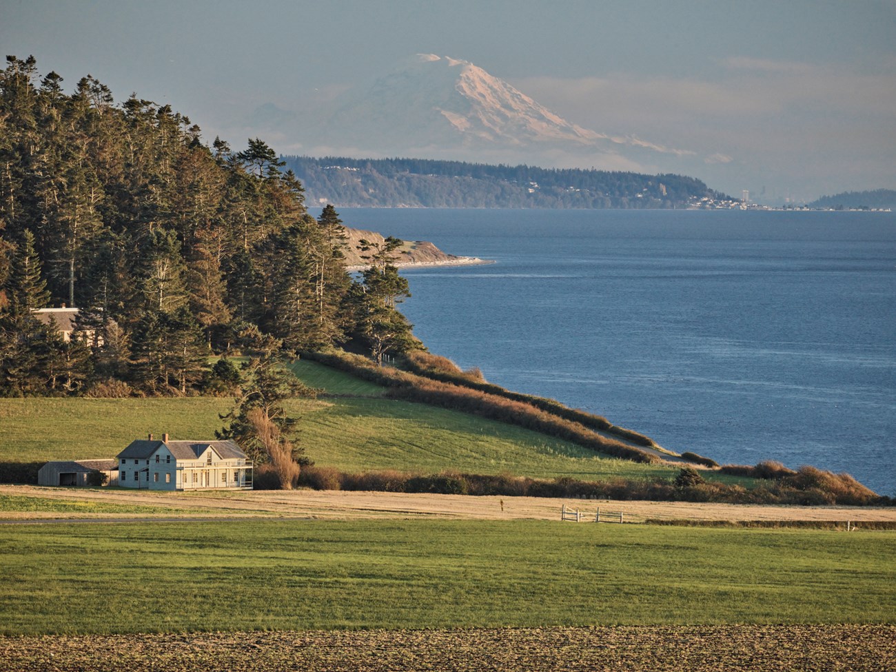 A house sitting in grassy fields with mountains and an ocean view in the background.