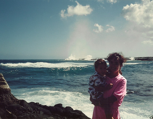 Mother and child standing in front of lava entering the ocean.