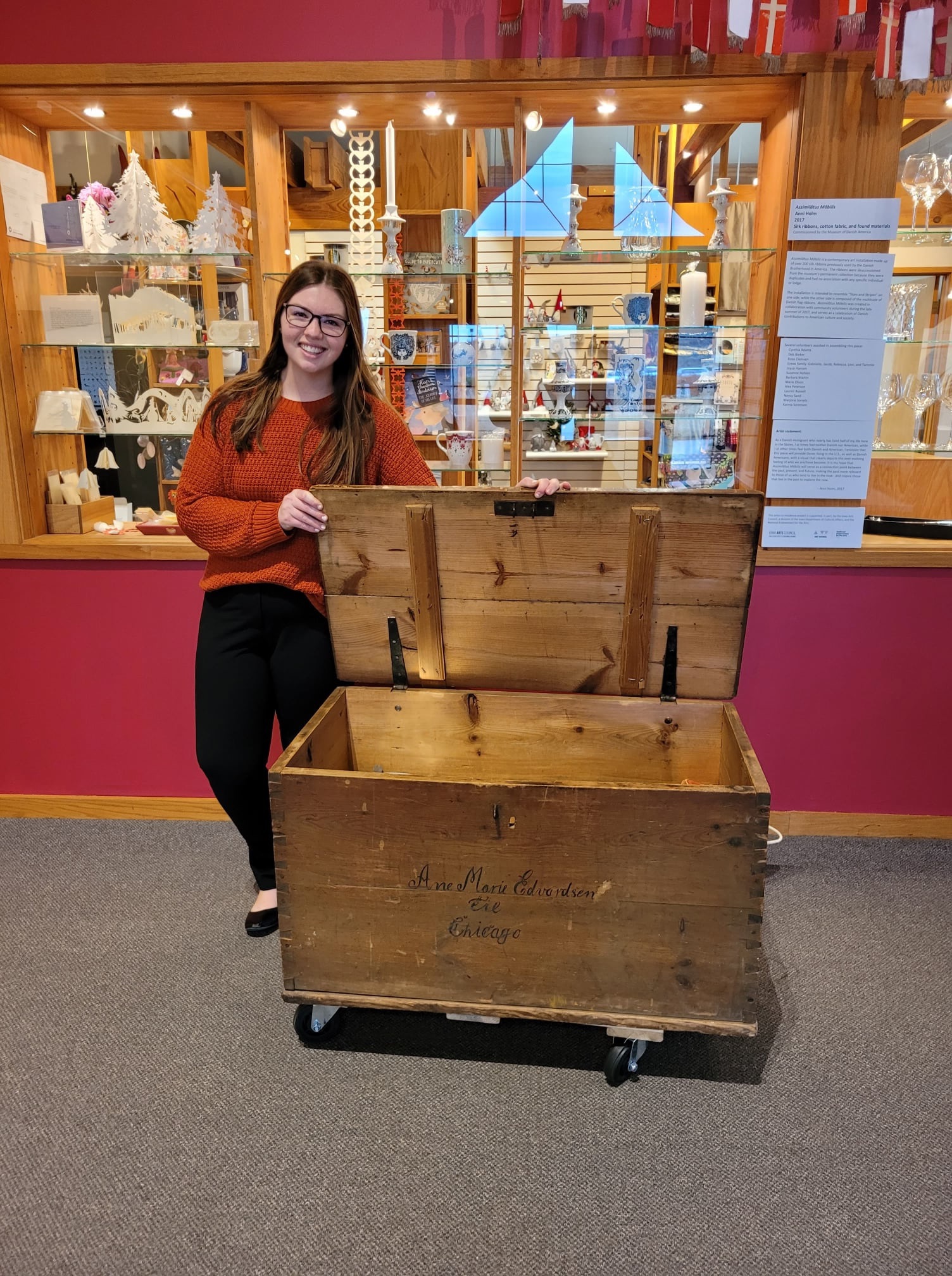 Hannah posing with a museum artifact behind a museum collection at the Museum of Danish America