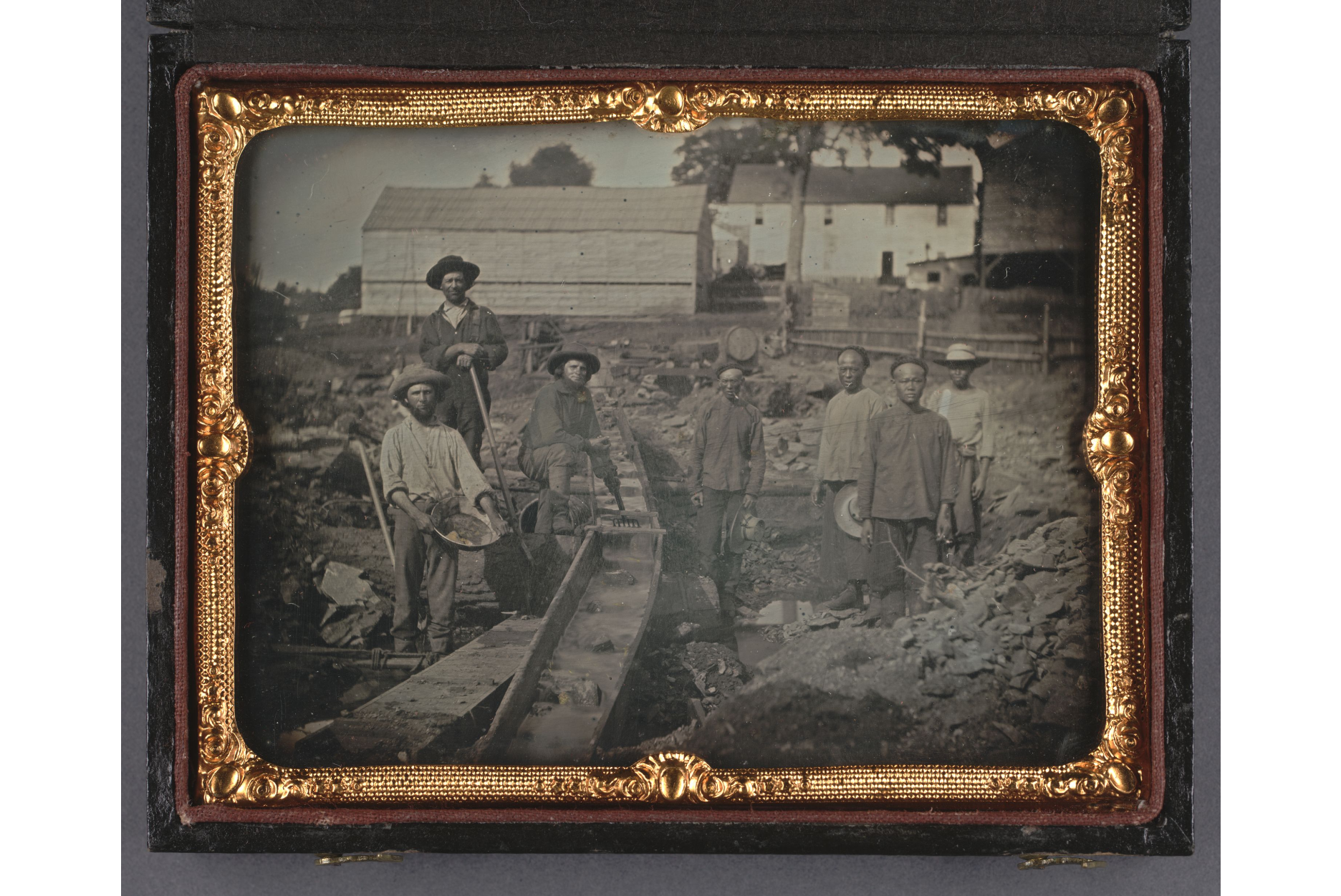 View of seven miners standing next to a sluice box; three white miners standing to the left of the sluice, four Chinese miners standing on the right.