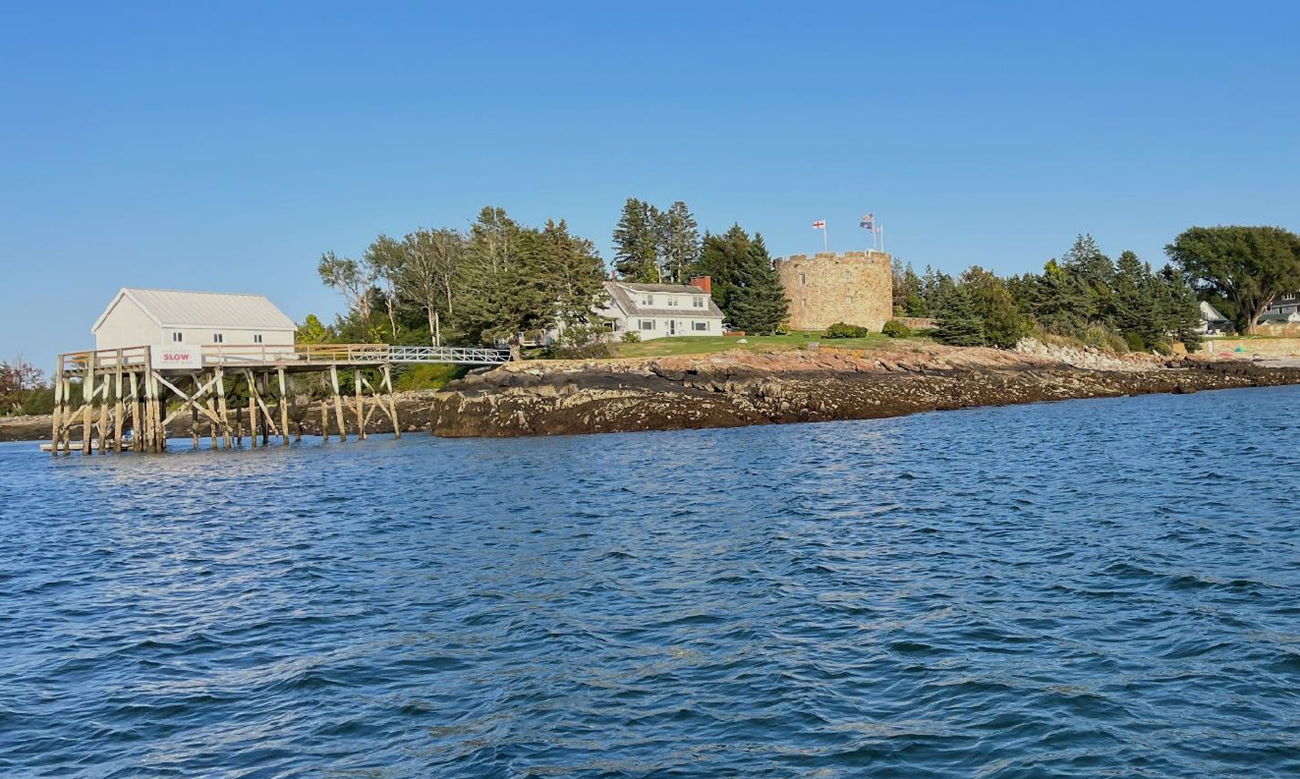 A rocky wooded island sits atop placid dark blue waters.