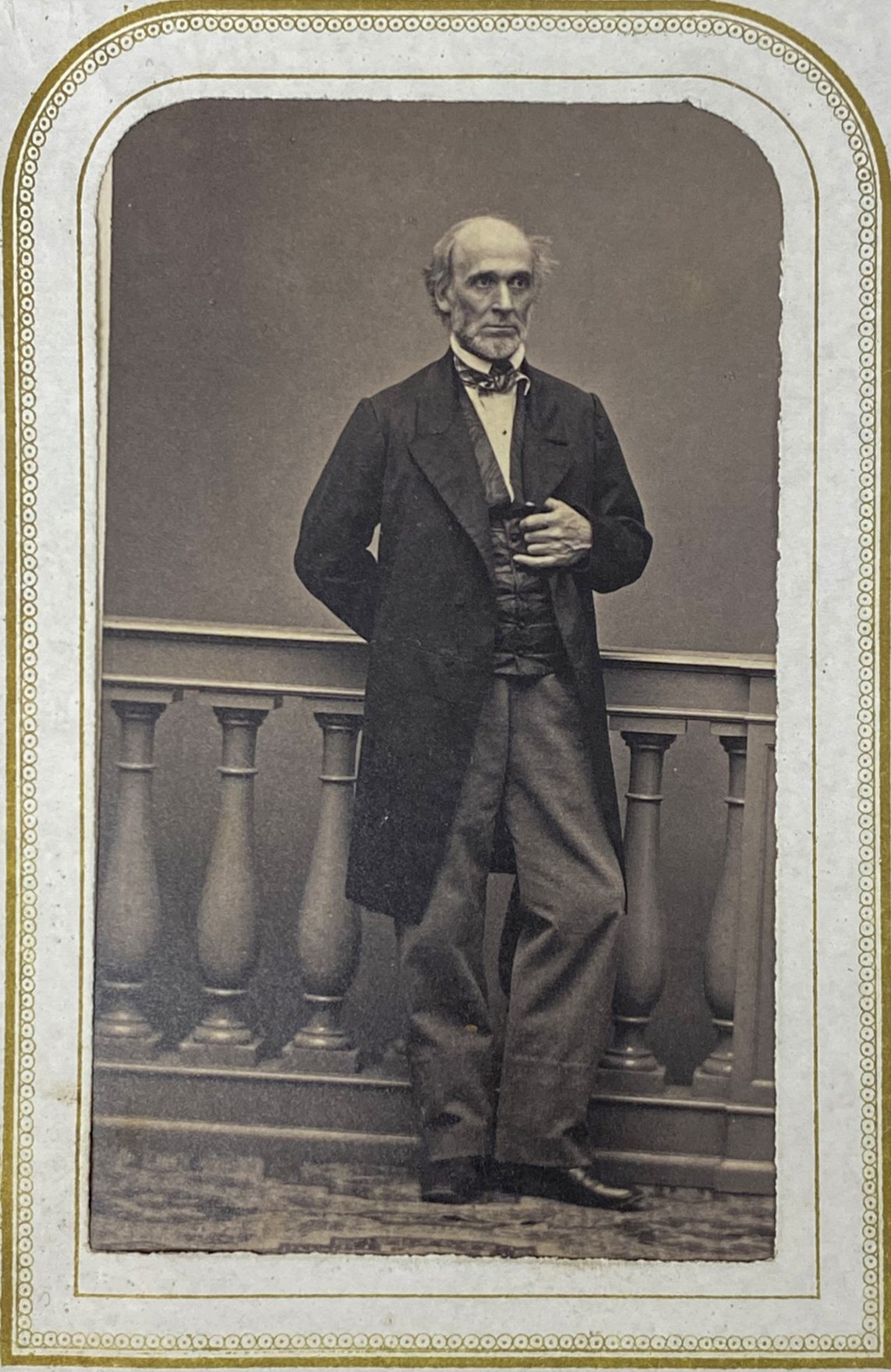 historic black and white photo of a tall, slender man in a long suit jacket, with gold colored frame