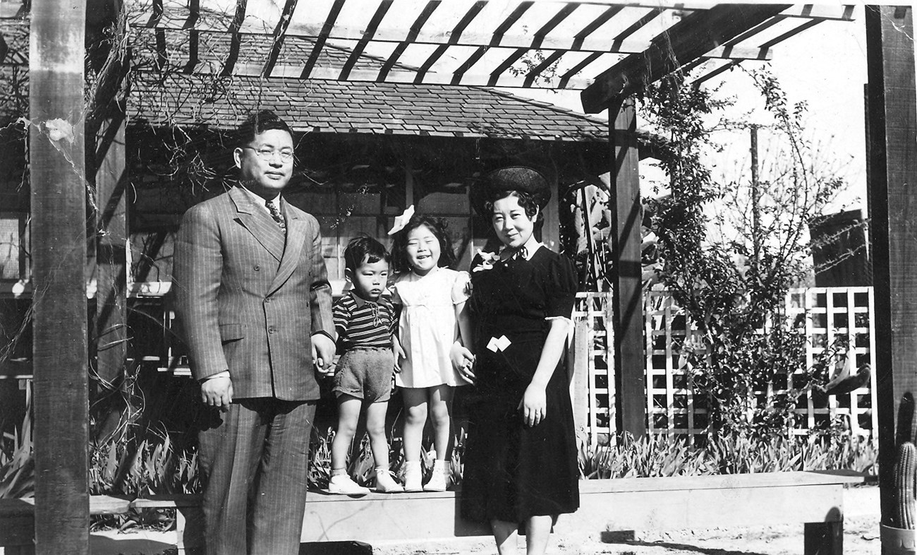 Black and white image of a family of four Japanese Americans standing in front of their house