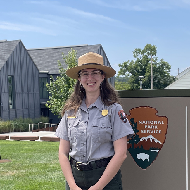 a woman wearing a NPS ranger uniform stands in front of a sign