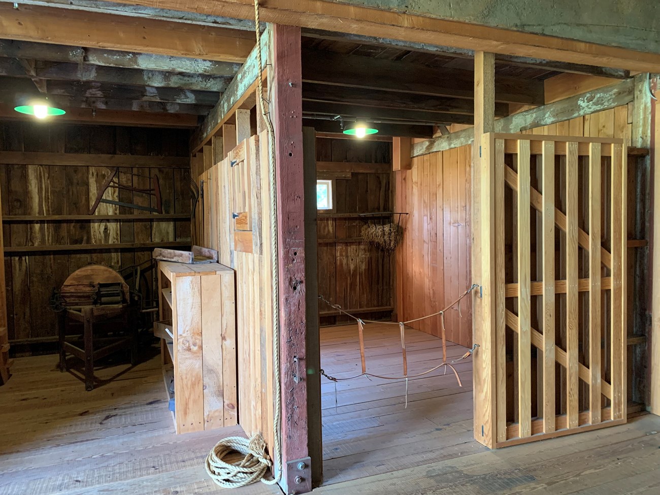 Two rooms inside a stable. The left room has a pitchfork and corn shucker. The right room is an empty stall for a horse.