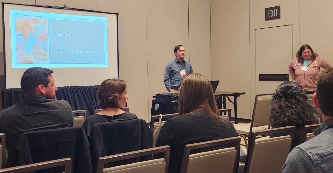 Man standing in front of room of people next to a projector screen