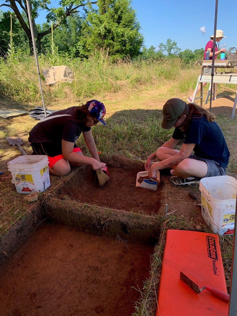 Two high school students work inside an archaeological pit.