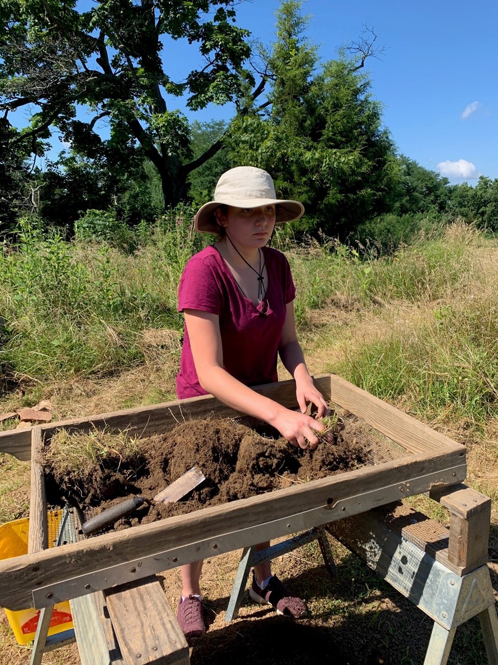 A high school student pushes dirt through a sieve as part of an archaeological study.