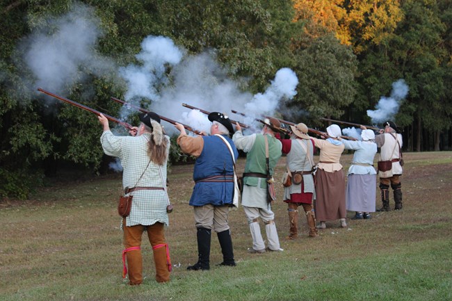 Reenactors stand in line and fire muskets