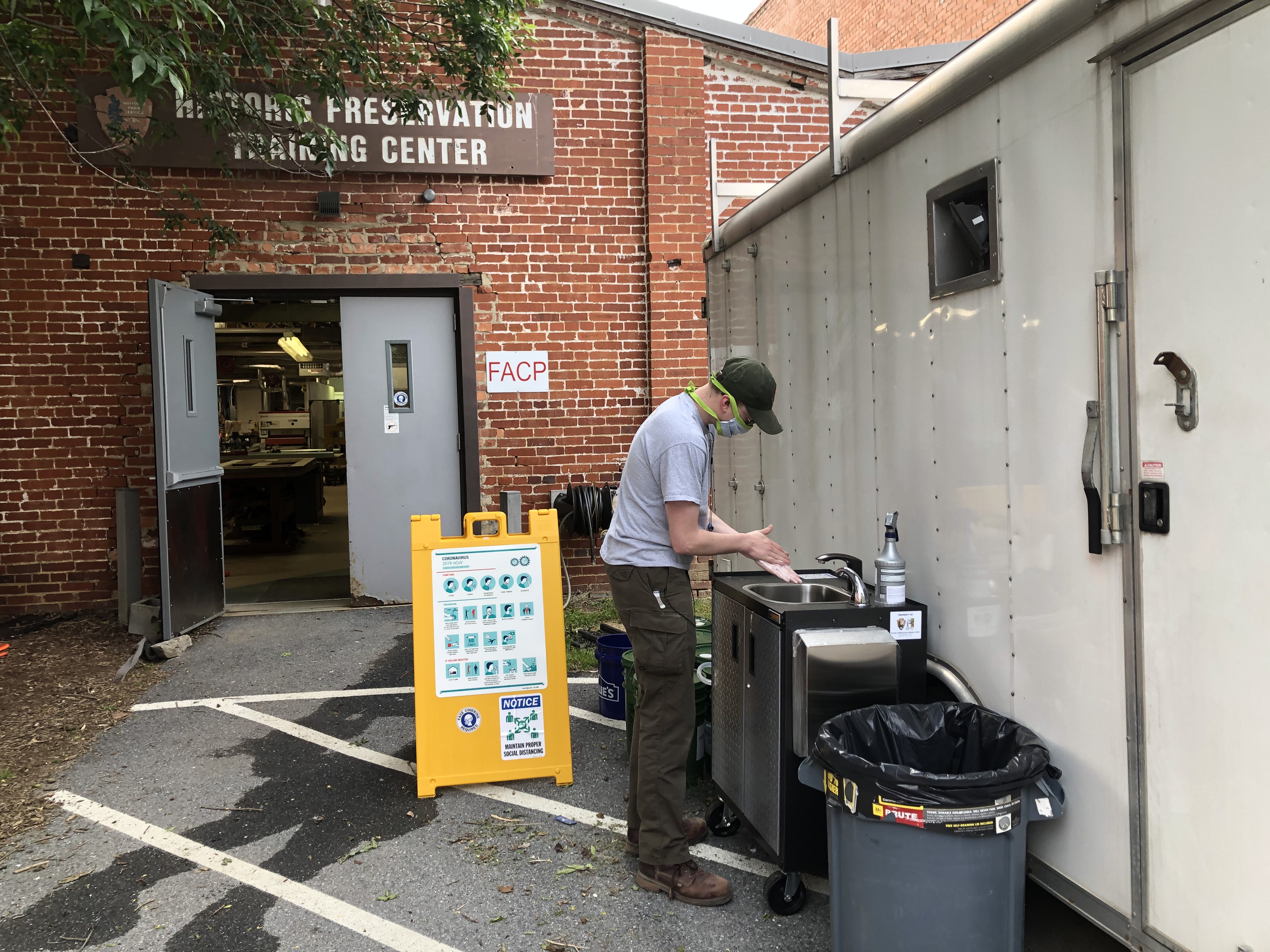 A worker wearing a cloth mask washes their hands in a mobile handwash station sink in a rolling cart.