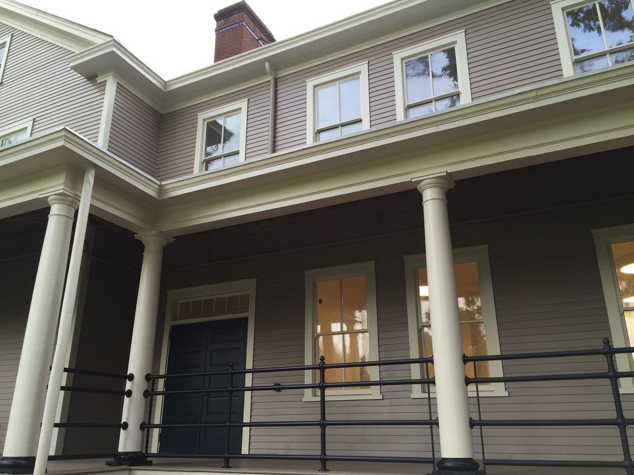 A portion of Building 987, a grey building with cream colored trim. Two stories are shown, with a large porch in the foreground.]