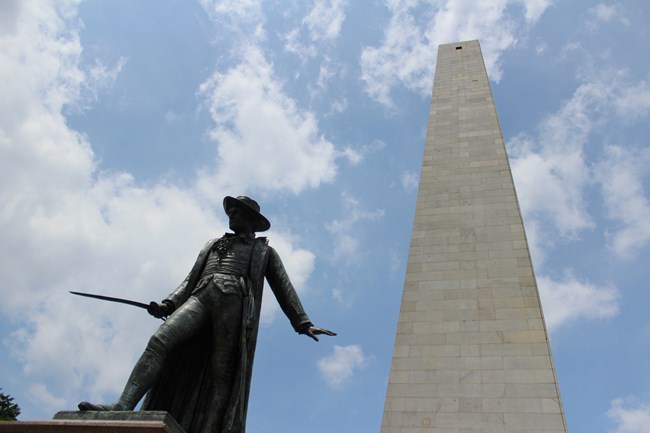 Angled photograph looking up at the Colonel Prescott Statue and Bunker Hill Monument.