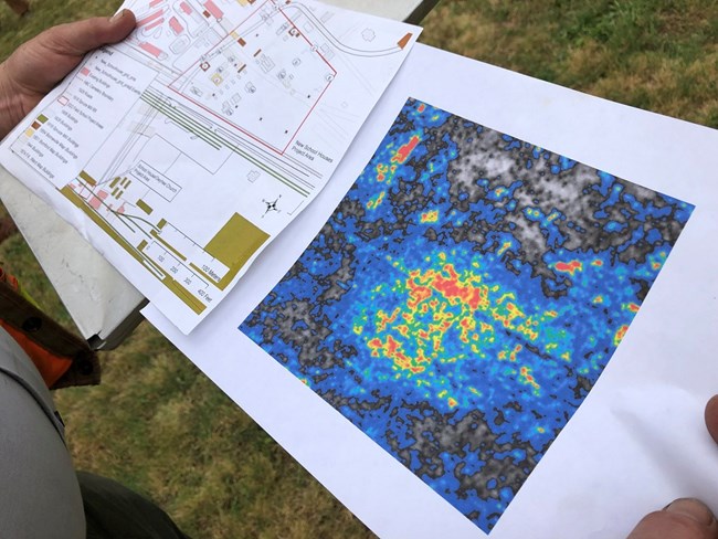 Hands hold a printout showing ground penetrating radar results. One one page is an image showing color coded areas in shades of blue, yellow, orange and red.