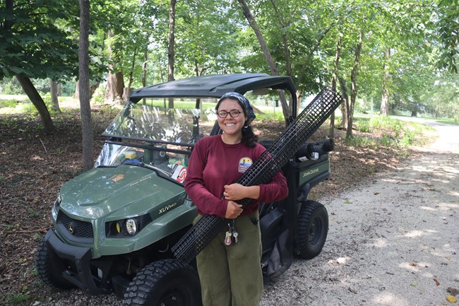 Madison, American Conservation Experience ACE Intern smiling big, holding tree protectors from deer