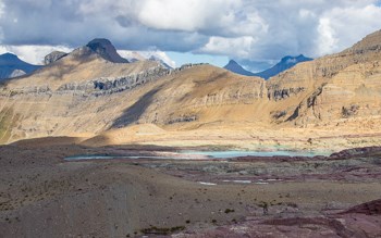 A wide angle image of a dry seeming alpine landscape with mountains in the background.