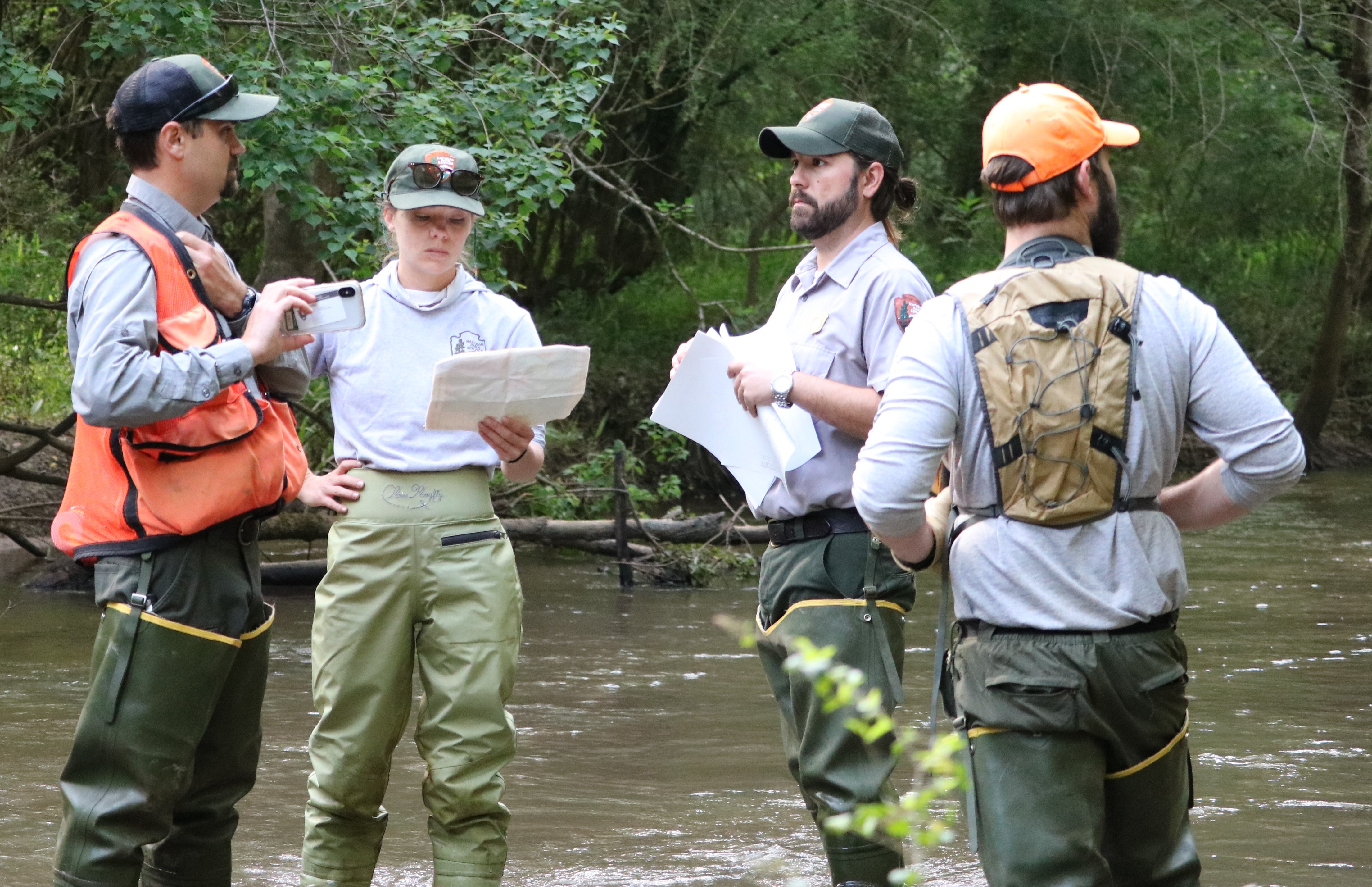 four people talking by a stream