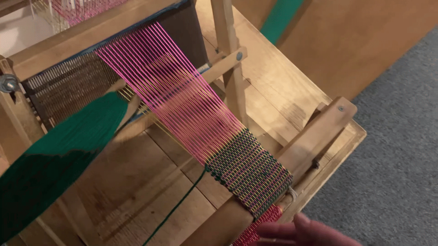 green yarn is passed through a "V" shaped opening of yellow and pink yarn