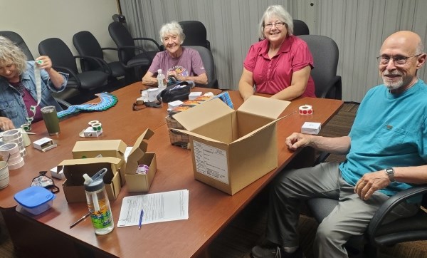 Four members of the Sticker Club sit around a table in an office with stickers.