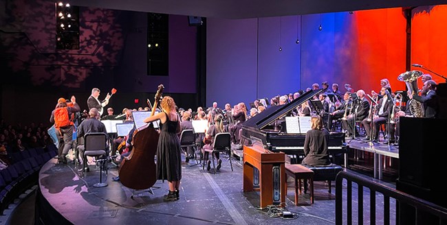 Keweenaw Symphony Orchestra performs a symphony commissioned for 85 years of Isle Royale, conductor holds fly swatter to comically swat mosquitoes