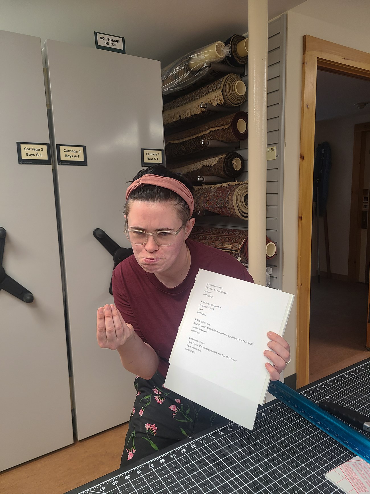 Curator looks at camera and makes a silly face while holding up a list of objects