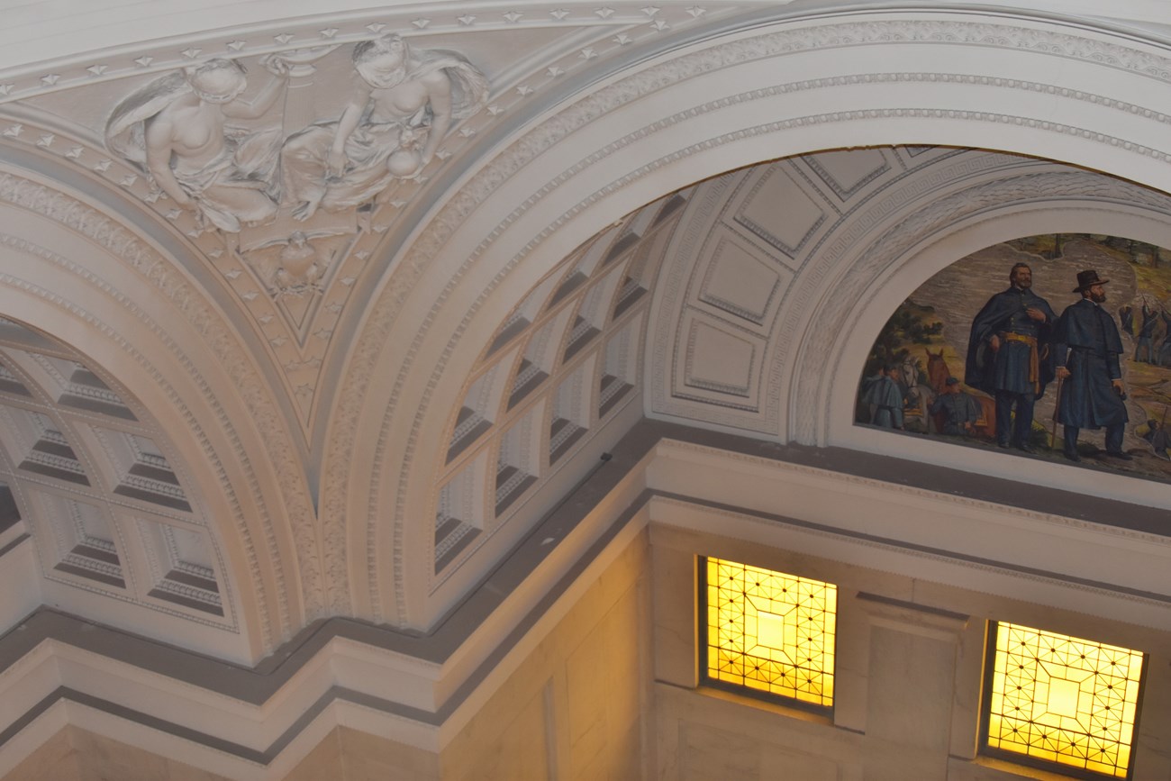 Photo of the interior of a mausoleum, featuring domed ceilings, white walls with architectural detailing, and a marble floor