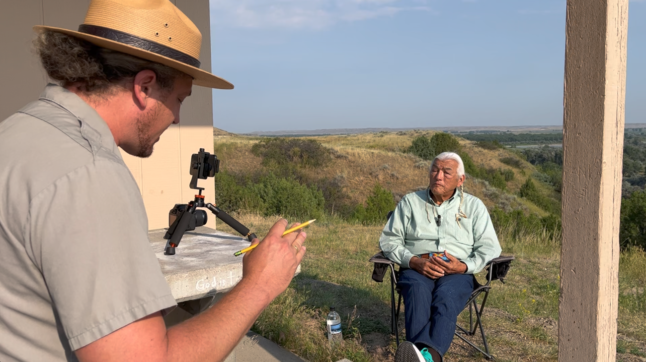 A man in a park ranger uniform interviewing a man sitting in a chair